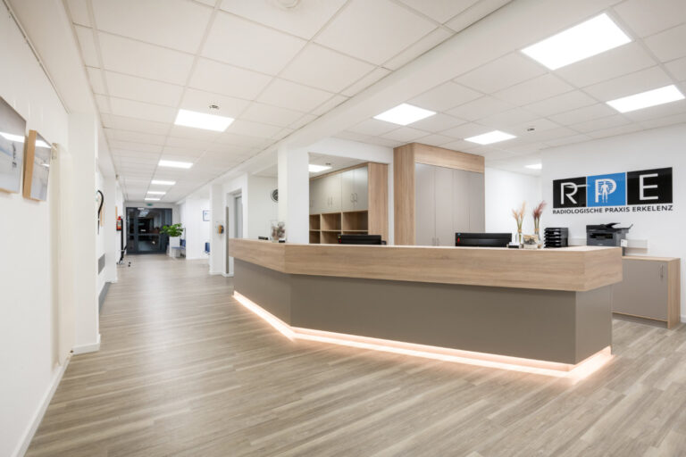 Moderner medizinischer Empfangsbereich der Radiologische Praxis Erkelenz mit einem Holzschreibtisch, Büroausstattung und der Aufschrift "Radiologische Praxis Erkelenz" an der Wand. Der Raum ist hell beleuchtet und hat ein klares, minimalistisches Design.