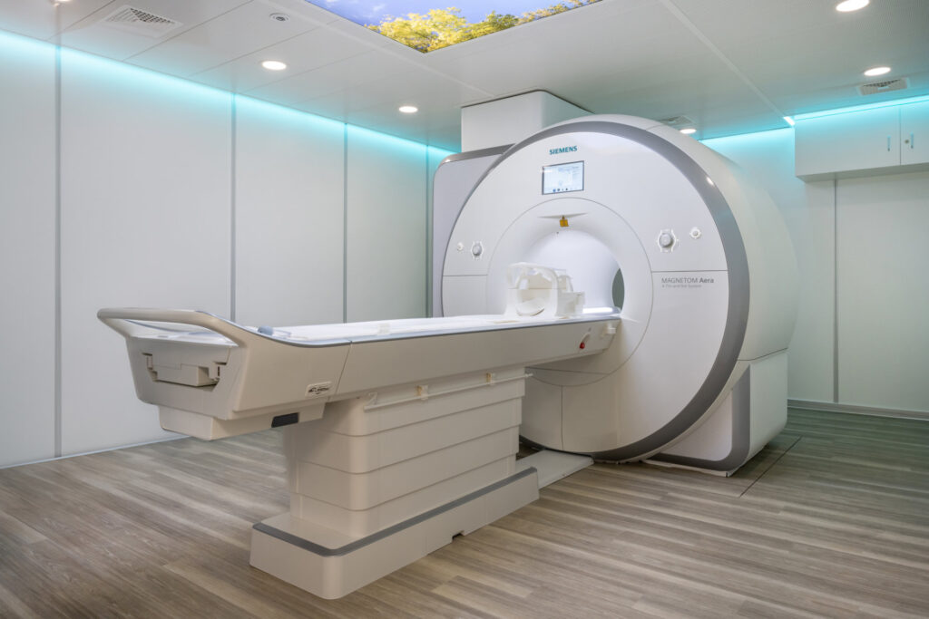 MRT-Gerät in einem sauberen, modernen Raum für medizinische Bildgebung mit Holzfußboden und Deckenbeleuchtung.