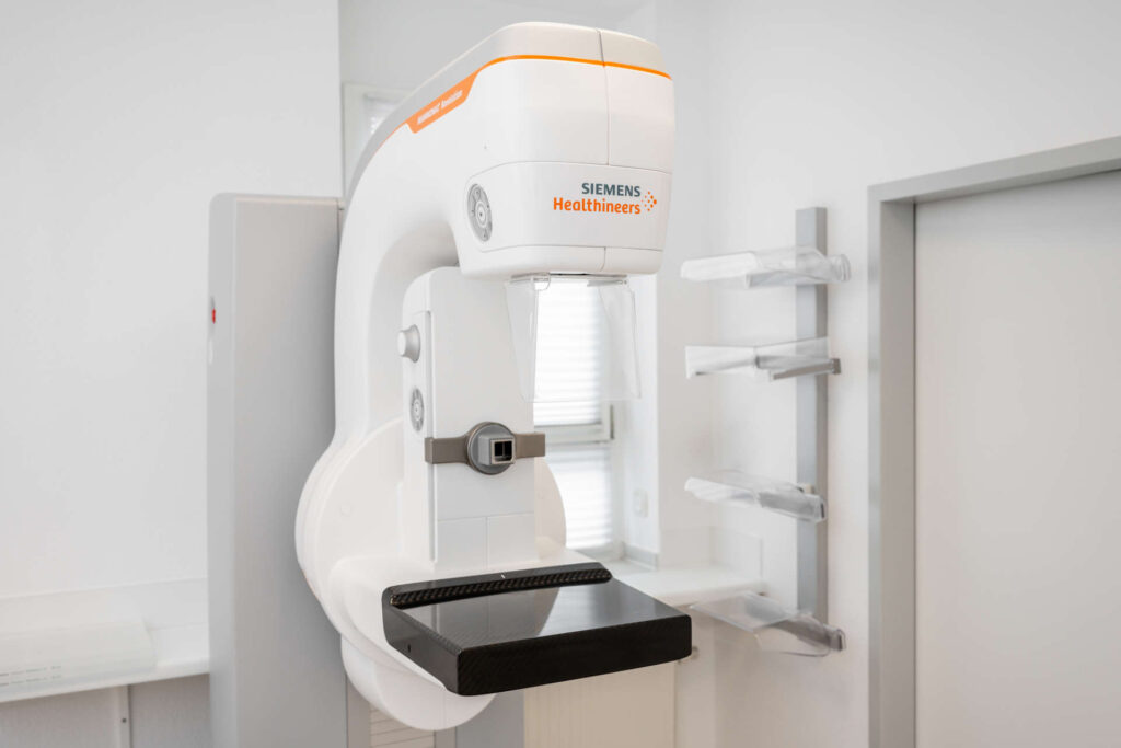 Ein Mammographiegerät von Siemens Healthineers mit einem Tablett zur Positionierung der Brust, Steuertasten und einem Bildschirm in einer klinischen Umgebung.