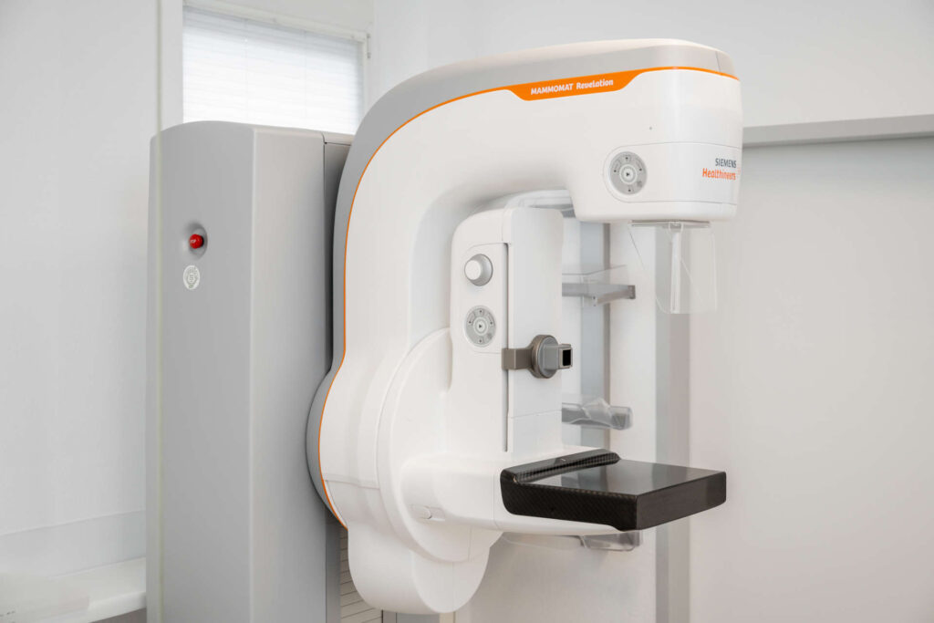 Ein Mammographiegerät von Siemens Healthineers mit einem Tablett zur Positionierung der Brust, Steuertasten und einem Bildschirm in einer klinischen Umgebung.