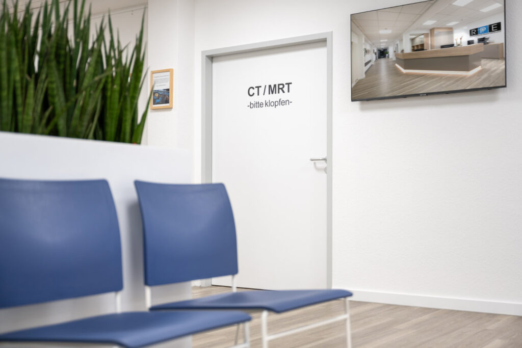 Wartebereich mit blauen Stühlen, einer Tür mit der Aufschrift 
